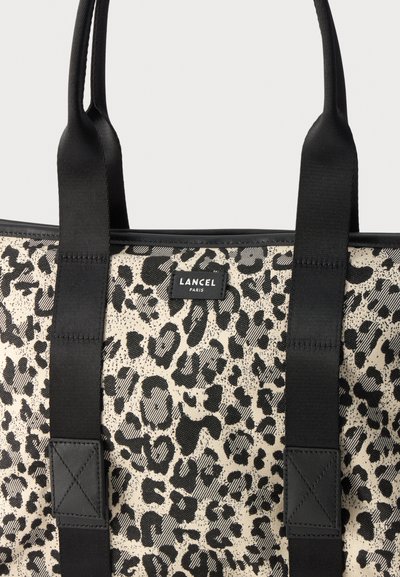 Крупен план на бежова чанта тип торба Lancel Paris с леопардова шарка в черно, дълги черни дръжки и пришити кожени подсилвания.