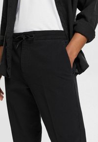 Czarne spodnie z lekkiego materiału, z elastycznym pasem i sznurkiem do wiązania, o smukłym kroju i bocznych kieszeniach.