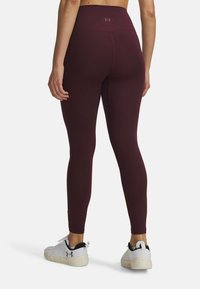 Burgunderfarbene, hochtaillierte Sportleggings aus einem glatten, dehnbaren Material. Mit kleinem Logo am Bund. Tragen zu weißen und schwarzen Turnschuhen.