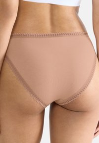 Beige bomulds-trusse med en gennemsigtig blondekant langs taljen og benåbningerne, med en glat tekstur og sømløst design.