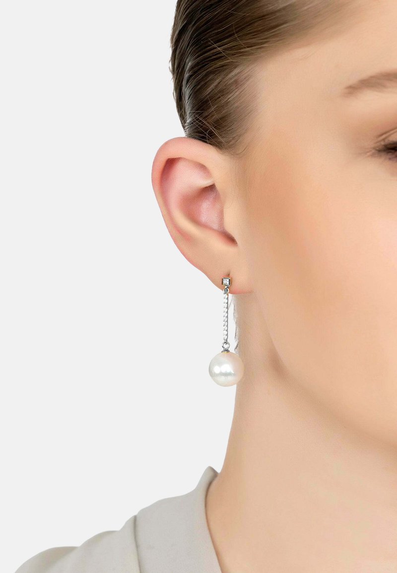 Pearl drop earrings with a silver chain and square stud. The pearl is glossy and round, hanging beneath the ear lobe.