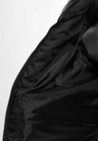 Czarna kurtka wewnątrz z gładką satynową podszewką, z zamkiem błyskawicznym i subtelnymi detalami przeszycia. Brak widocznych kieszeni lub wzorów.