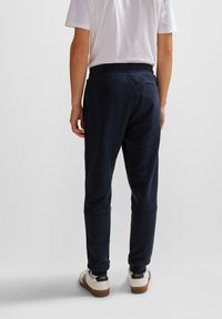 Navy joggers with a relaxed fit, cuffed ankles, and a back pocket, paired with a plain white T-shirt and white sneakers.