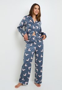 Ensemble de pyjama en soie avec un fond bleu-gris et un imprimé de grues blanches et roses. Le haut a un col et une fermeture à boutons ; le pantalon est ample.