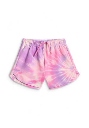 Dziewczyna z długimi włosami, ubrana w różowo-fioletową bluzę tie-dye i krótkie spodenki, trzyma różową butelkę na wodę i dopasowuje słuchawki.