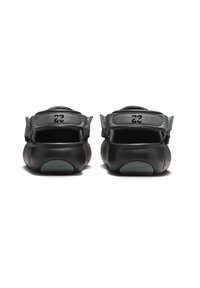 Svart fotbeklädnad med en slät lädertextur, med två justerbara remmar på baksidan och en distinkt logotyp ovanför hälen.