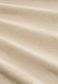 Țesătură bej cu un model subtil de frunze, având o textură netedă și o ușoară strălucire, evidențiind un aspect elegant și moale.