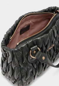 Borsa a mano in pelle nera con design trapuntato, cerniera in metallo dorato e fodera interna di un morbido rosa. Presenta una tracolla staccabile.