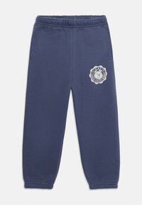 Marineblaue Sweatpants mit elastischem Bund, schmal zulaufenden Bündchen, seitlichen Taschen und einem weißen Logopatch mit einem Bärenemblem am linken Bein.
