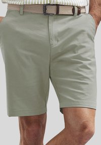 Khakifarbene Shorts aus leichtem Material, mit glatter Textur, seitlichen Taschen und geradem Schnitt. Akzentuiert mit einem gewebten Gürtel.