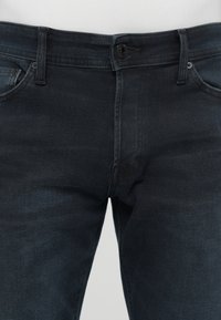 Vaqueros de mezclilla oscura con cierre de botón, pasadores para cinturón y bolsillos frontales. Textura suave con un ligero desvanecimiento, presentando un diseño clásico de pierna recta.