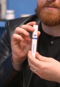 Vitt cylindriskt produkt med blå accenter och logotyp. Konisk design, hålls mellan fingrarna, med ett silverband runt mitten.