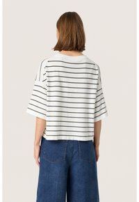 Hvid kortærmet top med grønne vandrette striber, der har en afslappet pasform og en bred halsudskæring, parret med blå denim bukser med vidde.
