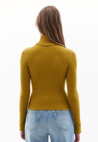 Musztardowy żółty sweter z prążkowanej dzianiny, z golfem i długimi rękawami, dopasowany fason, lekko skrócony dół. W zestawie z jasnoniebieskimi jeansami o wysokim stanie.