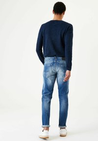 Suéter de punto azul oscuro y jeans de mezclilla azul claro con un ligero desvanecimiento. Zapatillas blancas con suelas beige. Diseño simple, corte relajado.