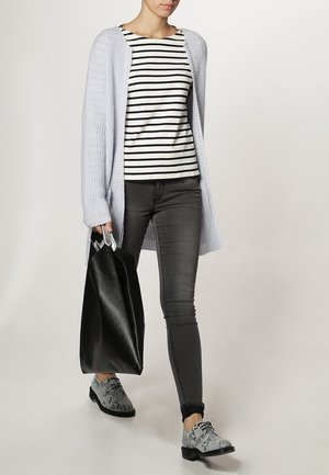 Light purple knitted cardigan over a striped black-and-white top, slim dark jeans, black bag, and patterned gray shoes.