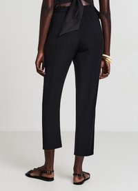 Pantaloni neri leggeri con vita elastica, lunghezza corta, gambe dritte e tessuto liscio. Abbinati a sandali piatti neri.