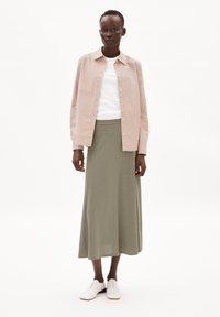Striped light pink button-up shirt over a white crew neck top, paired with a long olive green skirt and white lace-up shoes.