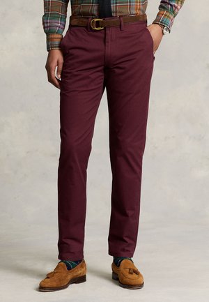 Homme portant un pantalon bordeaux, des mocassins en daim marron à pampilles, des chaussettes vert foncé à pois, une chemise à carreaux, une ceinture marron et une cravate noire.
