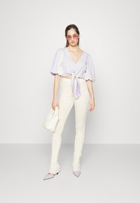 Top cropped em lilás claro com um padrão de diamante, calças brancas de cintura alta com bordas franzidas, sapatos apontados em lavanda e uma bolsa branca.