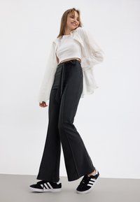 Pantalons larges à rayures noires et blanches, en tissu texturé, taille haute avec une ceinture à nouer, associés à un crop top blanc ajusté et des baskets noires.