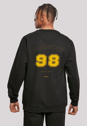 Black sweatshirt with yellow "BROOKLYN 98" print on the back. Features a crew neck and ribbed cuffs. Soft fabric, relaxed fit.