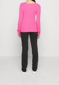 Růžový přiléhavý žebrovaný svetr se širokým výstřihem, doplněný tmavě šedými kalhotami a bílými teniskami, pohled zezadu.