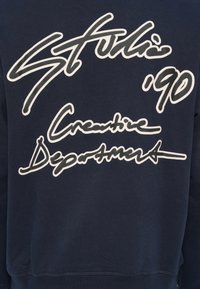 Μπλε σκούρο φούτερ με λευκό τυπωμένο κείμενο: "Stufii '90" κ αι "Creative Department" σε διαφορετικά στυλ. Μαλακή υφή και άνετη εφαρμογή.