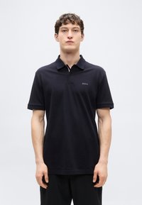 Μαύρο πόλο μπλουζάκι από βαμβάκι με κλασικό γιακά, κουμπιά και κοντά μανίκια. Διαθέτει διακριτικό λογότυπο "BOSS" στο στήθος.