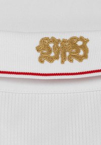 Tessuto a righe bianche con un logo ricamato dorato sul colletto, accentuato da una bordatura rossa lungo il bordo.