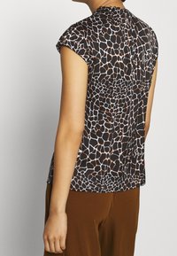 Blusa de manga corta con un estampado de jirafa en blanco y negro con acentos cobre; presenta un escote alto y una silueta suelta y fluida.