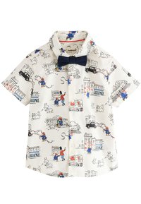Chemise blanche à manches courtes avec des scènes de Paddington Bear, des voitures noires, des chiens, des bâtiments et un nœud papillon bleu marine sur le col.