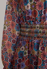 Section de robe à manches longues avec un motif floral coloré et une large ceinture élastique smockée, froncée avec de petites volants.