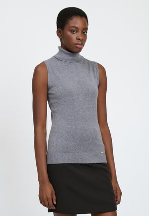 Pull encolure montant sans manches gris en tissu doux, avec un col et un ourlet côtelés. Porté avec une jupe noire.