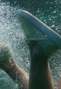 Deux jambes portant des baskets blanches se déplacent sous l'eau avec des bulles les entourant dans une eau claire.