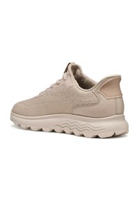 Scarpa sportiva beige con tomaia in mesh traspirante, superficie testurizzata, suola ammortizzata morbida e design ondulato. Presenta chiusura con lacci e linguetta sul tallone.