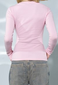 Light pink ribbed long-sleeve top with a fitted design, paired with high-waisted denim pants featuring dual back pockets.