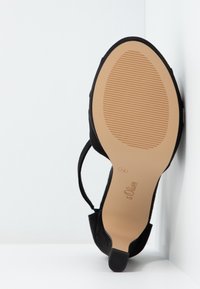 Chaussure à talon haut noire avec semelle beige, zone grip texturée, bride de cheville, et taille 38 marquée sur la semelle, placée contre un fond blanc en coin.