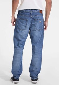 Jeans de mezclilla azul con un corte relajado, que cuentan con bolsillos traseros, un ligero desgaste y una etiqueta de cuero marrón en la cinturilla.