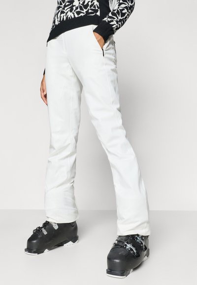 Bela smučarska hlače s tesnim krojem, z žepki na zadrgo in gladkim teksturo, v kombinaciji s črnimi smučarskimi škornji.