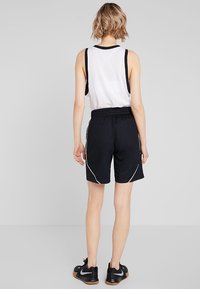 Pantalones cortos deportivos negros con cintura ajustable y costuras laterales blancas. Combinados con una camiseta sin mangas blanca con detalles negros. Calzado atlético visible.