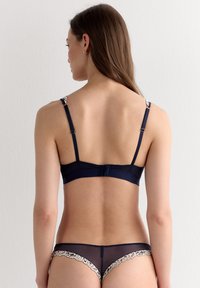 Ensemble de lingerie bleu marine comprenant un soutien-gorge à finition satinée, des accents de dentelle sur les bretelles, et un voile transparent en bas avec bordure en dentelle.