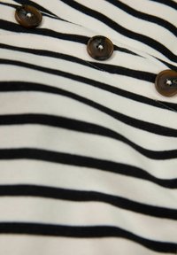 Randig tyg topp med horisontella svarta och vita ränder, rund bruna knappar och en mjuk textur.