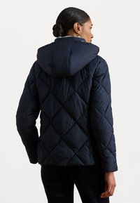 Námornícky prešívaný kabát s kapucňou, s diamantom prešívaním, mäkkou vnútornou podšívkou a priliehavým strihom. Vhodný pre chladné počasie.