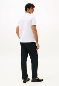 Camiseta blanca de manga corta combinada con pantalones oscuros de color navy. El modelo está posicionado de lado, mostrando un diseño simple y un ajuste casual.