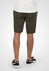 Olivgröna shorts i bomull med rak passform och sidofickor, tillsammans med svarta och guldiga sneakers.