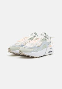 Zapatillas Nike que combinan colores blanco, verde pálido y melocotón, con parte superior de malla, acentos de ante suave y una unidad de aire visible en la suela.