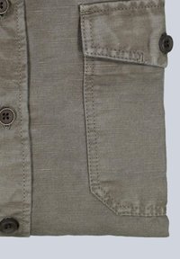 Grauer, strukturierten Stoff mit einer Knopfleiste mit zwei braunen Knöpfen und einer aufgesetzten Tasche mit Knopfdetail auf der linken Seite.