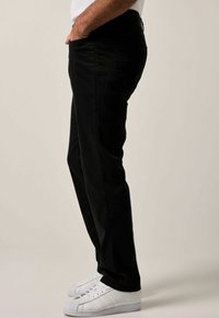 Pantalones negros de corte slim, confeccionados en una tela suave. Cuentan con bolsillos laterales y un diseño minimalista. Combinados con zapatillas blancas.