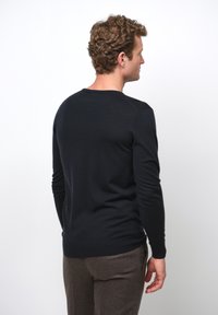 Svart långärmad stickad tröja med rund halsringning, tillverkad av mjukt material, med en åtsittande silhuett och ribbade ärmslut och kant.